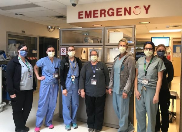 Emergency Room staff with masks on standing together under Emergency sign